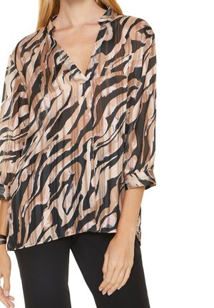 Kvinde iført en løs bluse med lange ærmer med et brunt, beige og sort abstrakt zebra print.