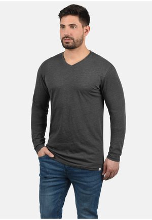 Camisa de manga larga con escote en V en tela gris oscuro, que presenta una textura suave y un ajuste relajado. Combinada con jeans azules.
