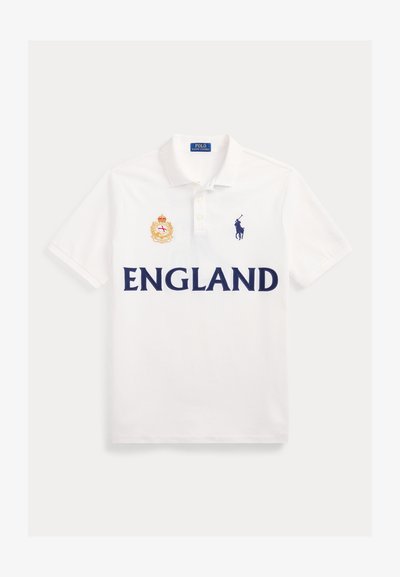 Λευκό πόλο μπλουζάκι με την επιγραφή "ENGLAND" σε σκούρα μπλε γράμματα, ένα κόκκινο και χρυσό έμβλημα στο αριστερό στήθος και το σκούρο μπλε λογότυπο Polo Ralph Lauren στο δεξί στήθος.