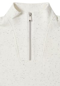 Haut zippé en tissu blanc cassé avec des taches noires ; possède un col haut et une fermeture éclair de quart à l'avant, texture lisse.