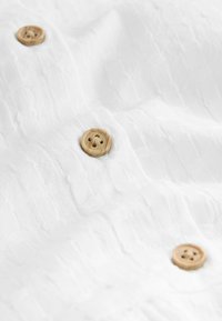 White textured fabric with several natural wooden buttons, displaying a four-hole design. Smooth surface with subtle pattern details.