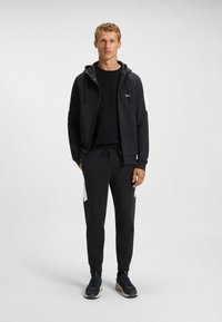 Black athletic outfit featuring a zip-up hoodie and jogger pants with white detailing. Made of soft fabric, designed for comfort.