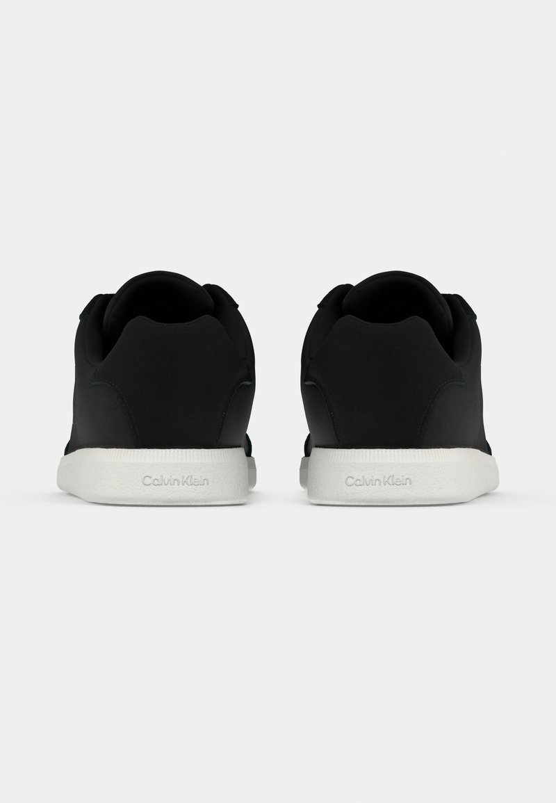 Black sneakers with a smooth upper, round toe, and a white textured rubber sole. Features a subtle logo on the heel.