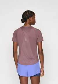 Αθλητική κοντομάνικη μπλούζα σε σκούρο μωβ, με διαφανή πλάτη από δίχτυ και διακοσμητικές γραμμές. Συνδυάζεται με ανοιχτό μπλε αθλητικά σορτς με λευκές λεπτομέρειες.