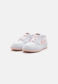 Nike tenisice s bijelim kožnim gornjim dijelom, ružičastim akcentima, okruglim vezicama i mekim ružičastim gumenom potplatom. Sadrži vidljivo šivanje i brendiranje.