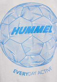 T-shirt blanc avec un graphisme bleu d'un ballon de football et des motifs de lignes ondulées, accompagné du texte "HUMMEL EVERYDAY ACTIVE" en bleu.