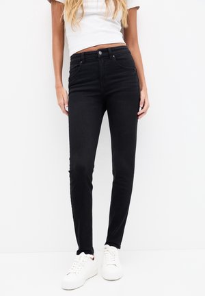 Jeans ajustados negros con tiro alto, fabricados en denim. Presentan bolsillos clásicos y trabillas para el cinturón, combinados con zapatillas blancas.