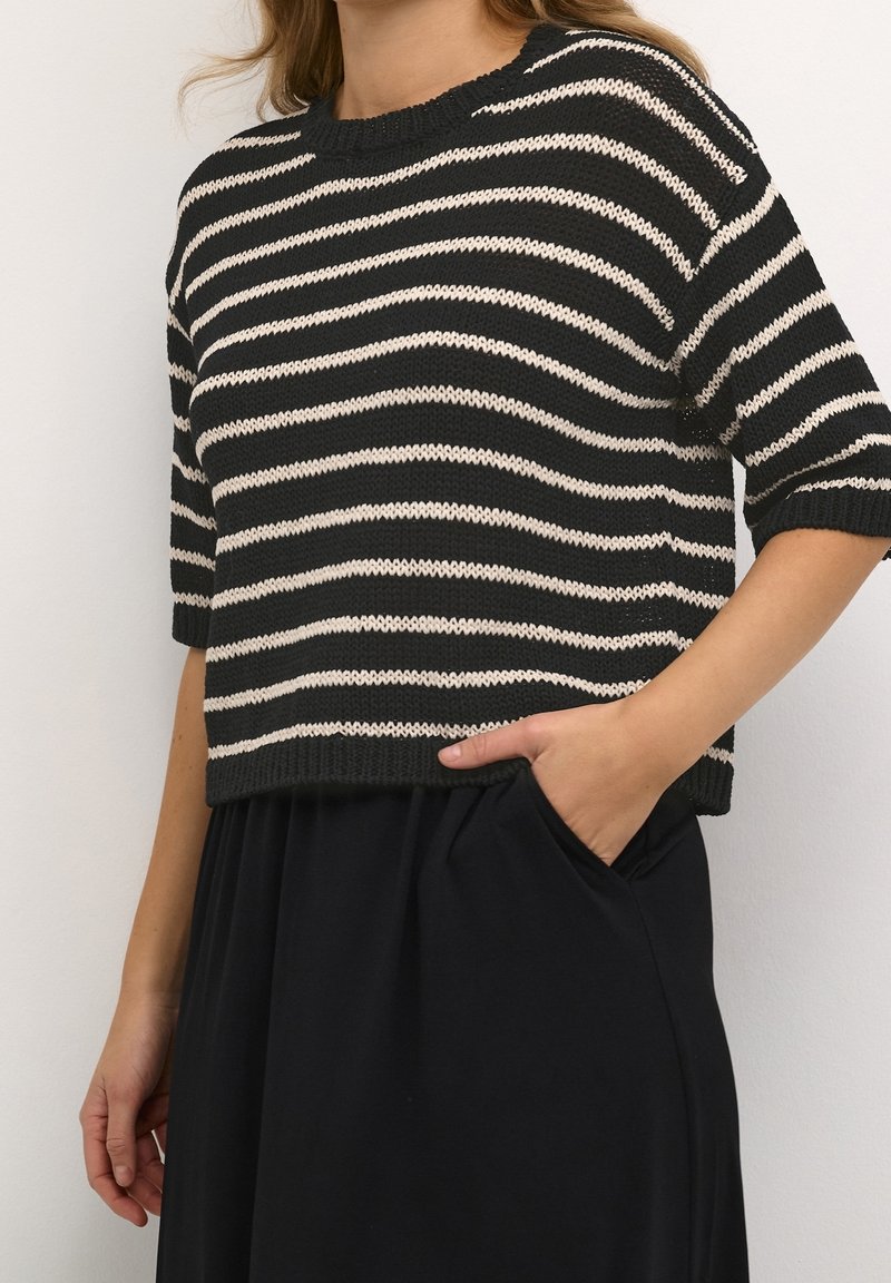 Strick-Crop-Top mit schwarz-weißen horizontalen Streifen, Rundhalsausschnitt, kurzen Ärmeln und lockerer Passform. Kombiniert mit einem schwarzen Rock.