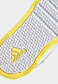 Suela de zapato Adidas, que presenta una superficie texturizada blanca con un patrón de panal, realzada por un borde amarillo y una etiqueta que dice "NO MARCA".