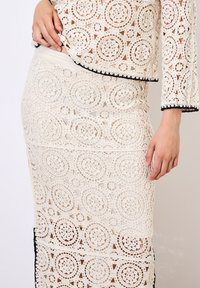 Ensemble en deux pièces en dentelle présentant des motifs circulaires complexes en crème avec des finitions noires, comprenant un haut court et une jupe jusqu'aux genoux.