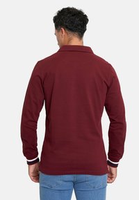 Polo de manga larga en burdeos con puños a rayas blancas y azul marino, cuello con solapa y diseño de color sólido. Fabricado en una suave mezcla de algodón.