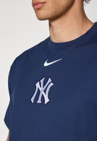 Námořní bavlnené tričko s vyšitým bielym a svetlomodrým logom Yankees a malým bielym Nike swooshom na golieri.