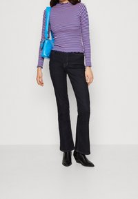 Paskowany top z długim rękawem w kolorze fioletowym i białym, z falbaniastym dołem, w zestawieniu z ciemnymi spodniami dzwonami i czarnymi botkami na obcasie. Akcesorium: niebieska torebka.