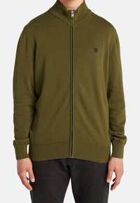 Suéter de cremallera color verde oliva con un cuello alto, puños y dobladillo acanalados, y un pequeño logo en el pecho. Fabricado con un material de punto suave.