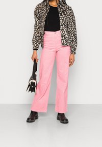 Lepardmönstrad knappjacka, ribbad svart topp, rosa kordfloddsbyxor med utsvängd ben, och svarta grova ankelskor, i kombination med en liten svart väska.