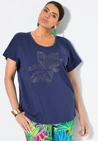 Mørkeblå t-shirt med korte ærmer og et blomstermotiv lavet af metalnitter, kombineret med farverige, mønstrede blomsterbukser.