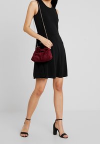 Musta hihaton mekko, joka on yhdistetty kerättyyn burgundin väriseen mokkahanneuliin ja mustiin korokepolkkaisiin sandaaleihin. Handbagissa on ketjuhihna.