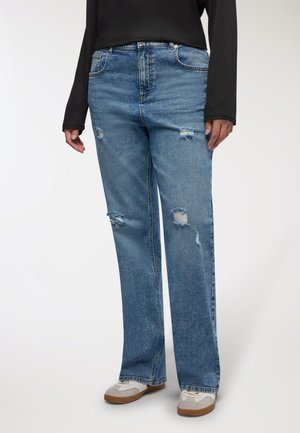 Jeans azzurri chiari strappati con una vestibilità a gamba dritta, caratterizzati da zone sfilacciate e decorazioni minime, abbinati a scarpe da ginnastica grigie.