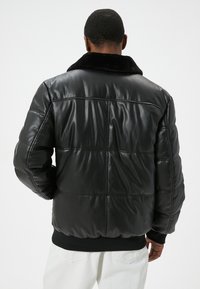 Veste puffer en cuir noir avec un col en fausse fourrure doux, design matelassé, ourlet côtelé et texture lisse, vue de dos.
