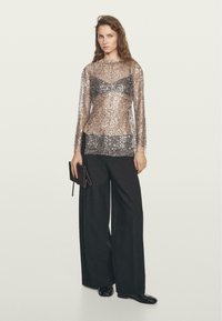 Top a maniche lunghe in tessuto trasparente con paillettes argento, abbinato a pantaloni neri a gamba larga e una pochette nera.