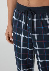 Navy-karierte Schlafanzughosen mit weicher Textur, elastischem Taillenbund mit Kordelzug und einem karierten Muster in weißen und roten Linien.