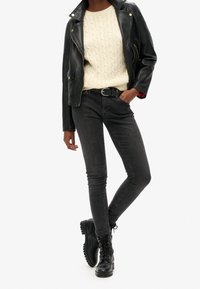 Black leather biker jacket, cream cable-knit sweater, black skinny jeans, and black lace-up boots. Smooth textures and fitted design.