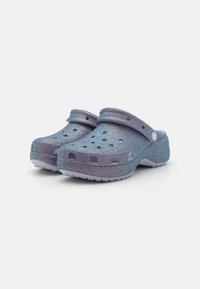 Cizme din material ușor, de culoare albastră strălucitoare, cu orificii de ventilație, curea în spate și o talpă texturată pentru aderență.