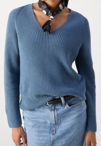 Pull en tricot côtelé bleu avec col en V et manches longues, associé à une jupe en jean clair et une écharpe noire nouée autour du cou.