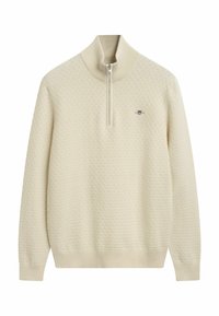 Crème-kleurige gebreide pullover met hoge kraag en kwart-ritssluiting; heeft een textuurpatroon en een klein logo op de borst.