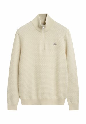 Crème-kleurige gebreide pullover met hoge kraag en kwart-ritssluiting; heeft een textuurpatroon en een klein logo op de borst.
