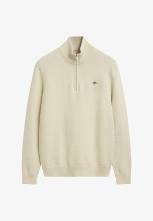 Cremefarbener Strickpullover mit hohem Kragen und Viertelreißverschluss; verfügt über ein strukturiertes Muster und ein kleines Logo auf der Brust.