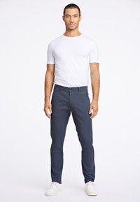 T-shirt bianca in cotone abbinata a chinos blu navy slim-fit e sneakers bianche. L'outfit presenta un design semplice e classico, senza motivi visibili.