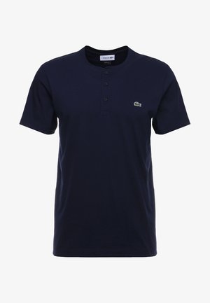 T-shirt henley bleu marine à manches courtes avec trois boutons et petit logo crocodile vert sur le côté gauche de la poitrine.