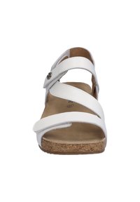 White sandal with multiple wide straps and adjustable buckle, cork footbed, and flat sole. Smooth synthetic material and soft inner lining.