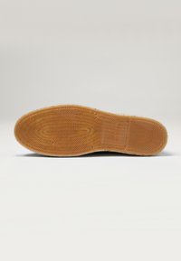 Suela de zapato con un patrón de goma texturizado. El color es marrón claro con un diseño geométrico, presentando un borde suave y un detalle de logo.