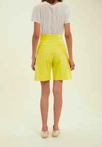 Shorts en coton jaune avec taille haute, poches latérales et boutons à l'arrière, accompagnés d'une chemise blanche à manches courtes.