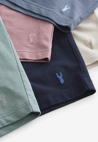 Cinco camisas de manga corta en varios colores: verde, rosa, azul marino, gris y beige, con pequeños motivos bordados de ciervos en los dobladillos.