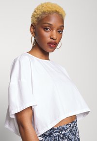 T-shirt branca cropped com mangas curtas, feita de um tecido suave, combinada com uma saia azul estampada, apresentando um corte solto e um ajuste casual.