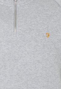 Pullover grigio a mezza zip realizzato in tessuto morbido e testurizzato. Caratterizzato da una zip argento e un piccolo logo giallo ricamato sul petto.