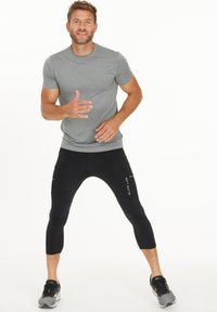 Sportoutfit für Herren, bestehend aus einem grauen Kurzarmshirt und schwarzen Capri-Leggings. Die Leggings haben Reißverschlüsse und weiße Akzente.
