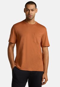 Rostfarbiges T-Shirt mit kurzen Ärmeln, Rundhalsausschnitt und Taschen auf der linken Brust. Weicher Stoff und lässige Passform.
