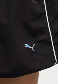 Shorts noirs avec un détail de passepoil blanc et un petit logo Puma réfléchissant près de l'ourlet au-dessus de la jambe d'une personne.