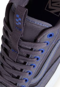 Baskets gris foncé avec œillets et coutures bleues, texture en tissu et daim, lacets épais et languette à tirer sur la langue.