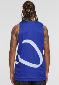 Canotta in rete blu con grande design grafico bianco sul retro. Presenta ampi fori per le braccia e una vestibilità ampia.
