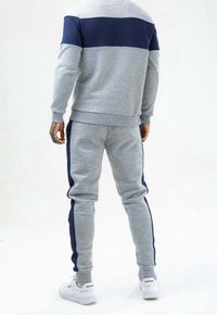 Szary hoodie i dresy z granatowymi akcentami. Materiał wydaje się miękki; projekt zawiera blok kolorów na górze i paski po bokach spodni.