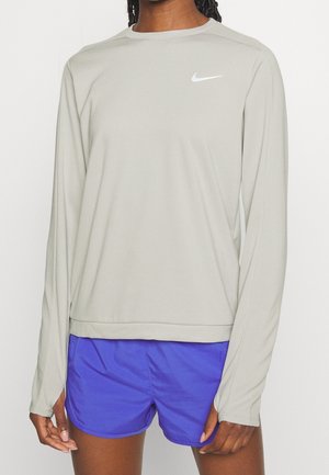 Lichtgrijs sportshirt met lange mouwen en een ronde halslijn, voorzien van een wit Nike-logo op de borst, gecombineerd met blauwe shorts. Glad, lichtgewicht materiaal.