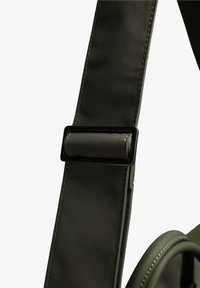 Correa de hombro de color verde oliva, hecha de nylon texturizado, con una hebilla de metal negro y costuras reforzadas a lo largo de los bordes.