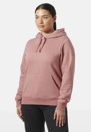 Sudadera rosa con capucha hecha de tela suave, con bolsillo tipo canguro, cordones y puños acanalados. Se lleva con vaqueros oscuros.