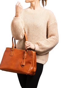 Borsa in pelle color tan con manici doppi, forma rettangolare e cuciture a contrasto; tenuta da una persona che indossa un maglione beige con texture.