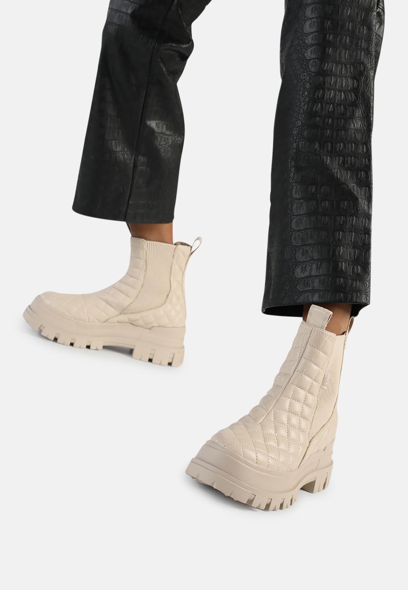 Bottines beiges matelassées avec semelles épaisses à relief portées avec un pantalon court en similicuir noir.